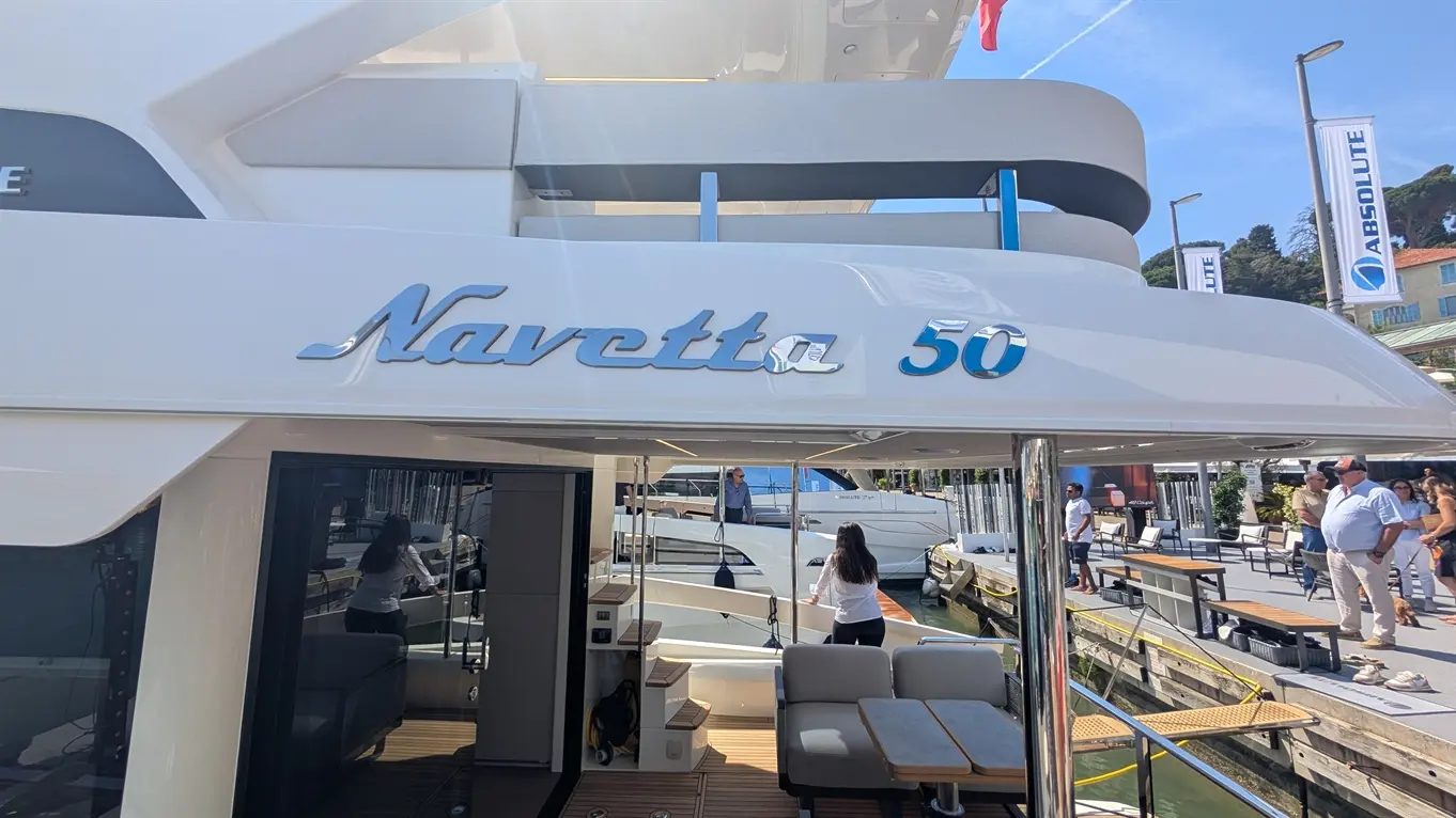 Navetta 50 yacht displayed at a marina, featuring a sleek design, outdoor seating, and people examining the boat.
